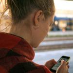 blonde woman holding phone at train station