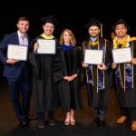 four men pose with a woman in graduation regalia