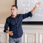 man in blue button up pointing at a white board