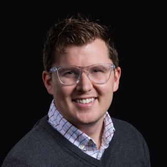 headshot of Andrew Reddie, smiling, black background