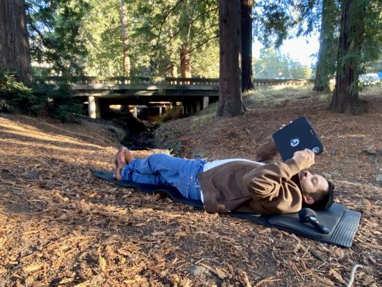 man laying down in a forest with a tablet in hand